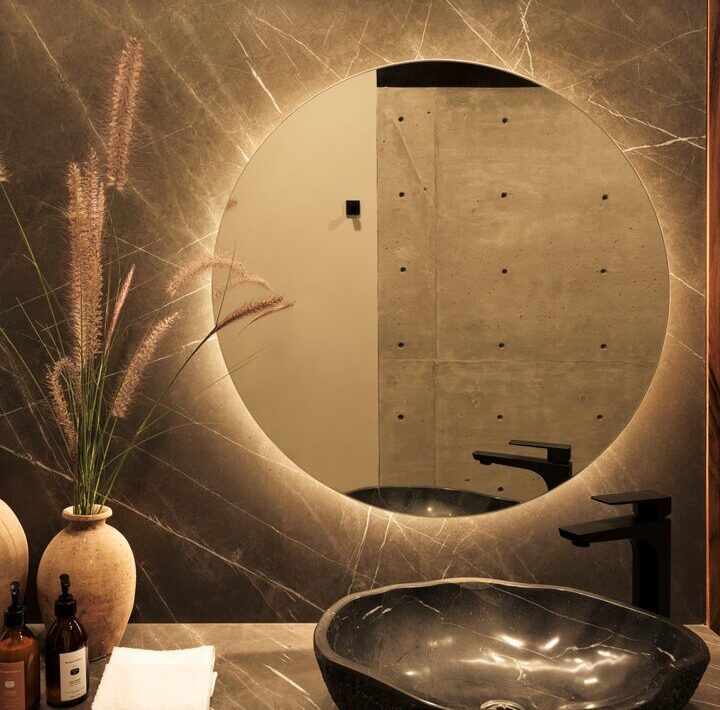 Baño de Casa Kerany con espejo circular retroiluminado y lavabo de piedra