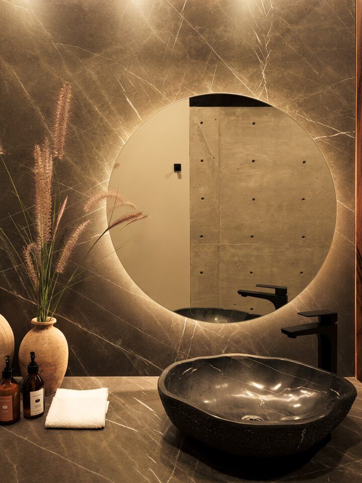 Baño de Casa Kerany con espejo circular retroiluminado y lavabo de piedra