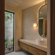 Baño de Casa Mikelín con espejo circular, lavabo de piedra y muros de cemento pulido