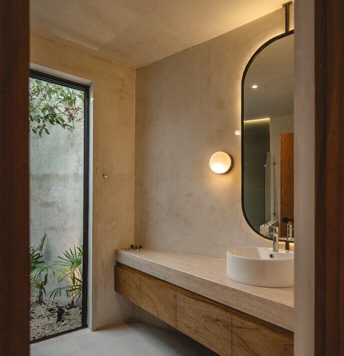 Baño de Casa Mikelín con espejo circular, lavabo de piedra y muros de cemento pulido