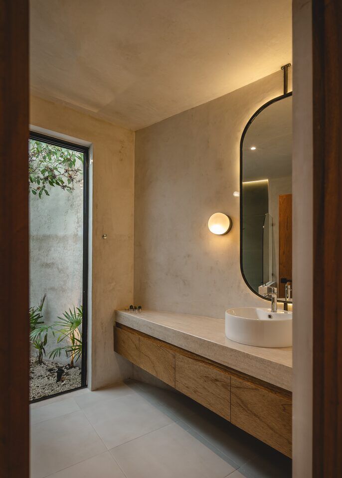 Baño de Casa Mikelín con espejo circular, lavabo de piedra y muros de cemento pulido