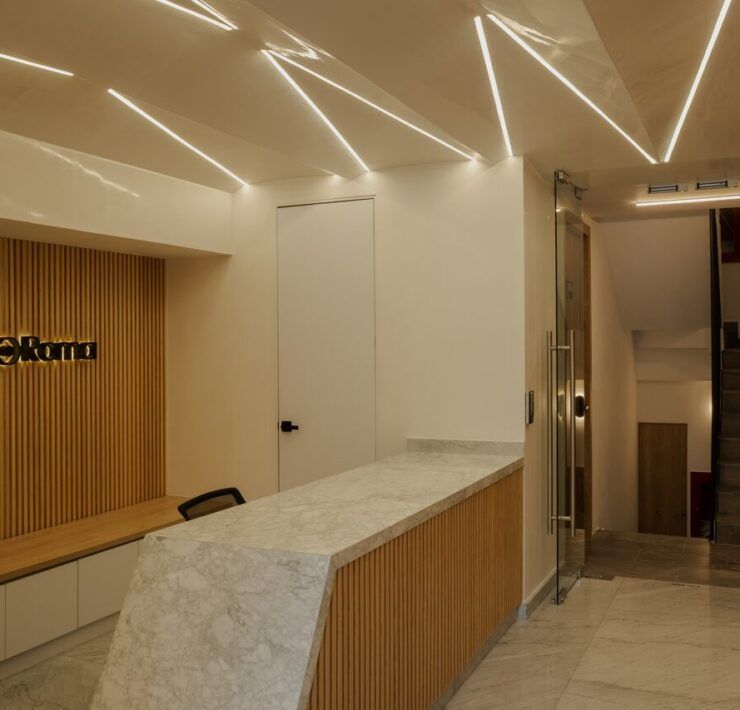 Lobby de Casa Roma 350 con plafones triangulares iluminados y recepción