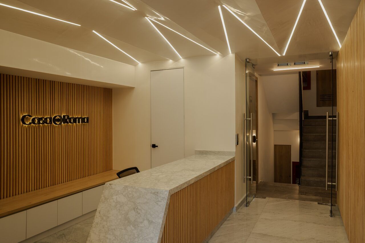 Lobby de Casa Roma 350 con plafones triangulares iluminados y recepción