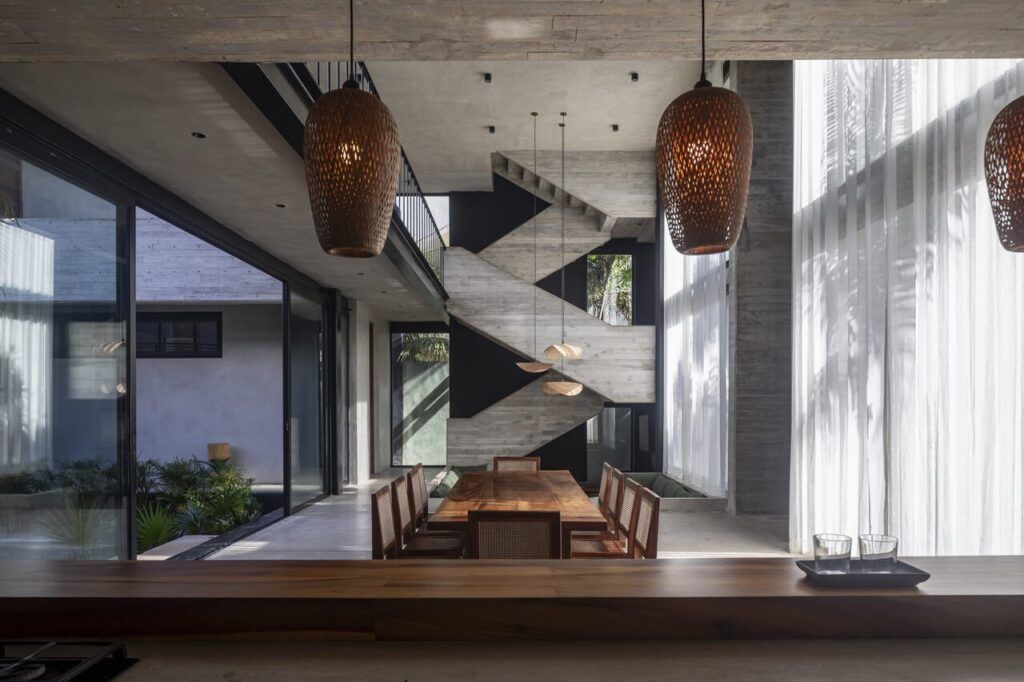 Comedor a doble altura de Casa Vihara con lámparas artesanales y cortinas que filtran la luz