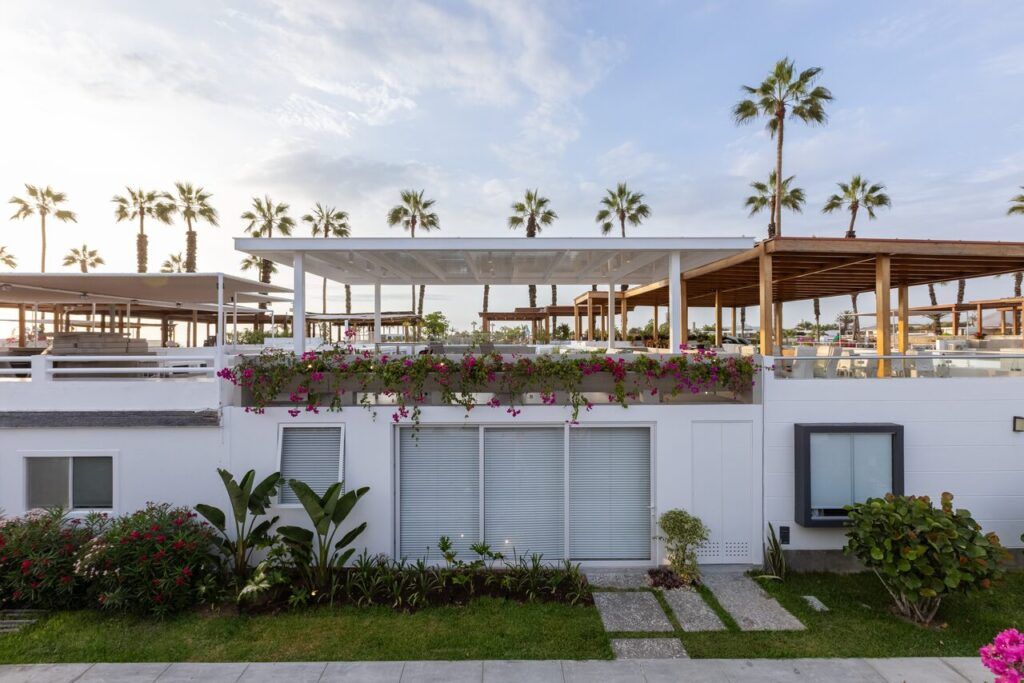 Fachada blanca de Casa Martinica con jardín, bugambilias y palmeras del balneario