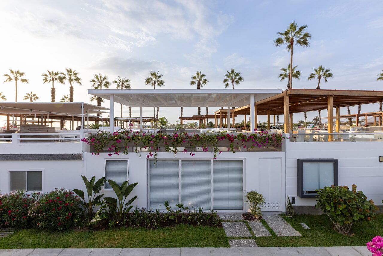 Fachada blanca de Casa Martinica con jardín, bugambilias y palmeras del balneario