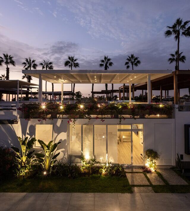 Fachada de Casa Martinica iluminada de noche con jardín
