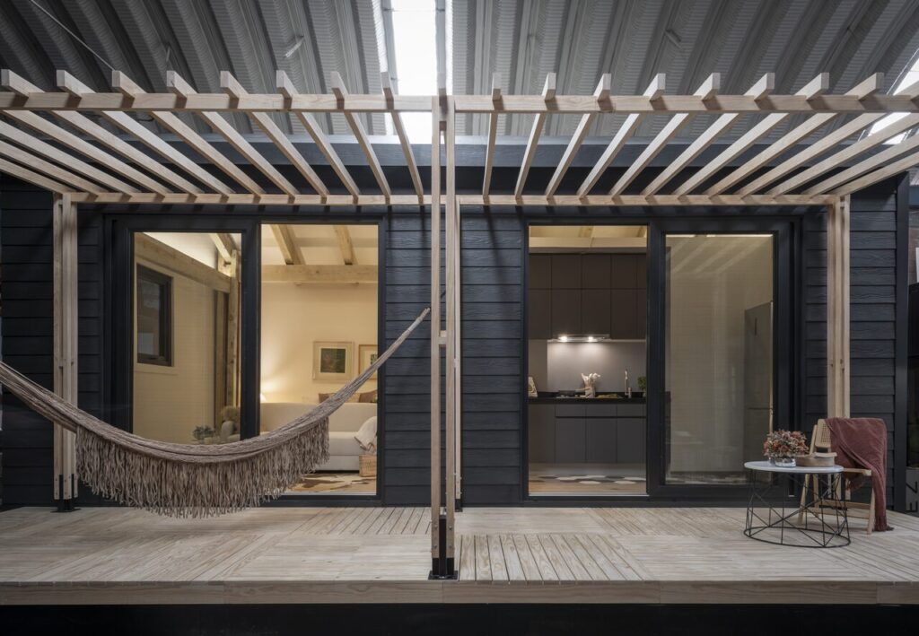 Casa Yoli iluminada de noche con pérgola, hamaca y ventanales