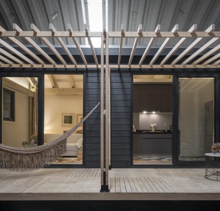Casa Yoli iluminada de noche con pérgola, hamaca y ventanales