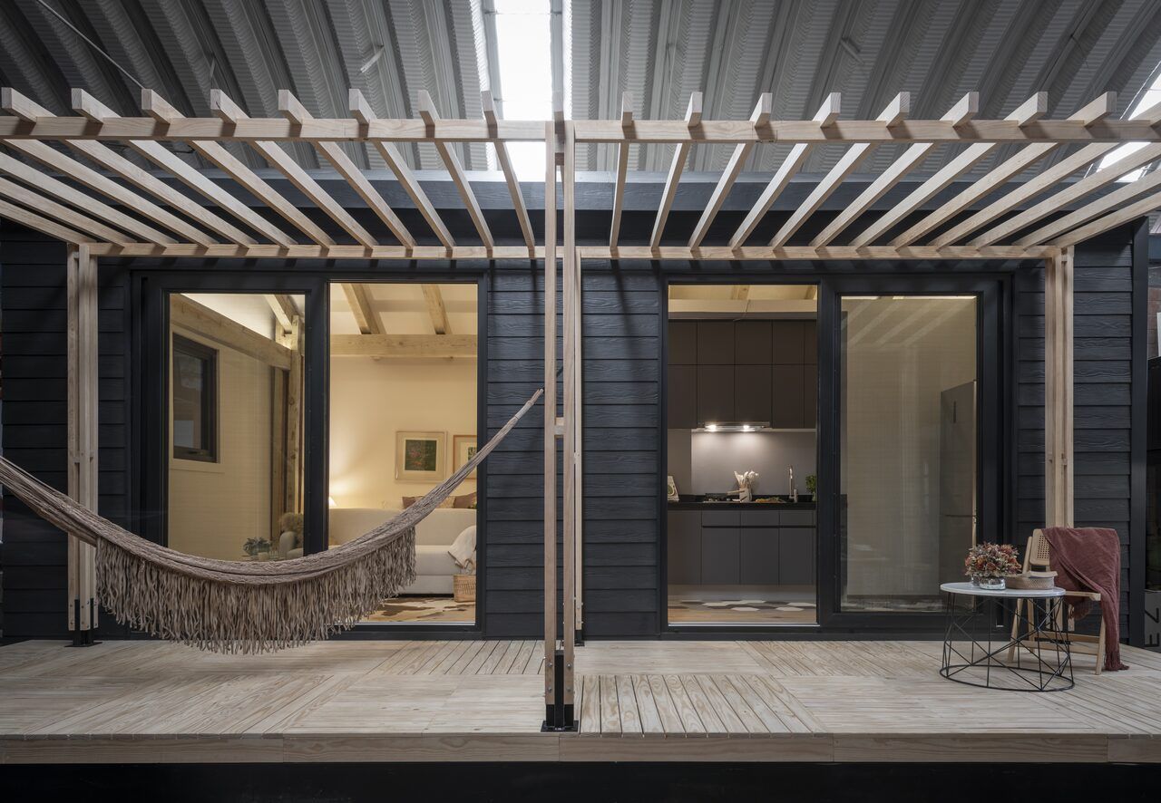 Casa Yoli iluminada de noche con pérgola, hamaca y ventanales