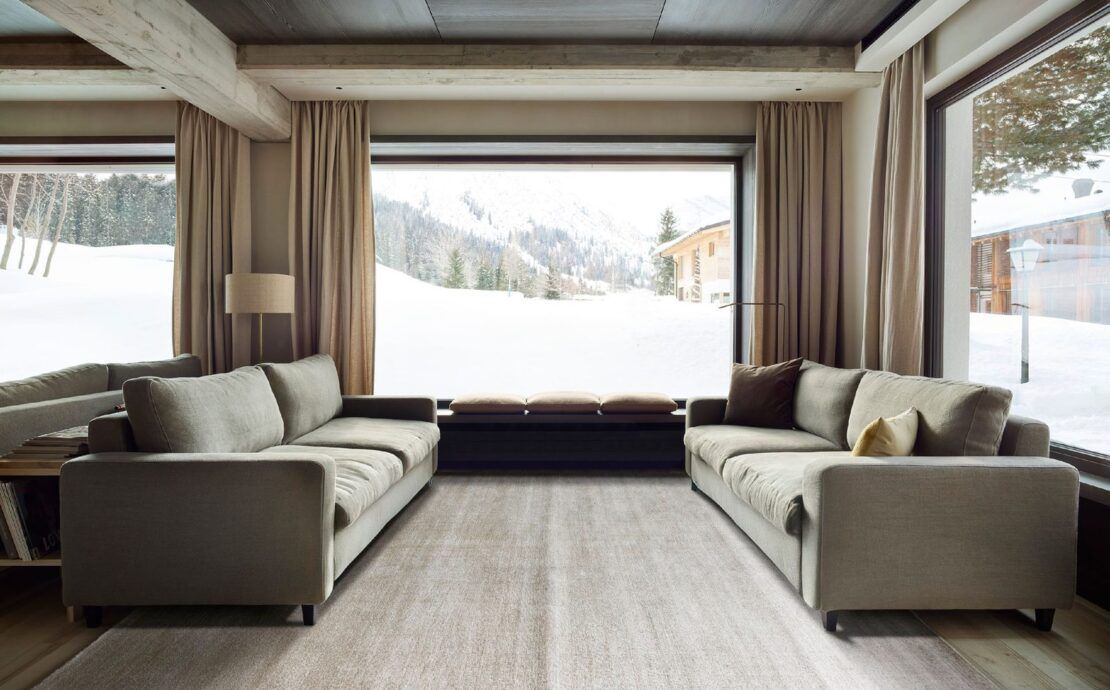 Alfombra Frizzantino de G.T.DESIGN en tono gris perla en una sala de chalet con dos sofás y ventanales con vista a la nieve