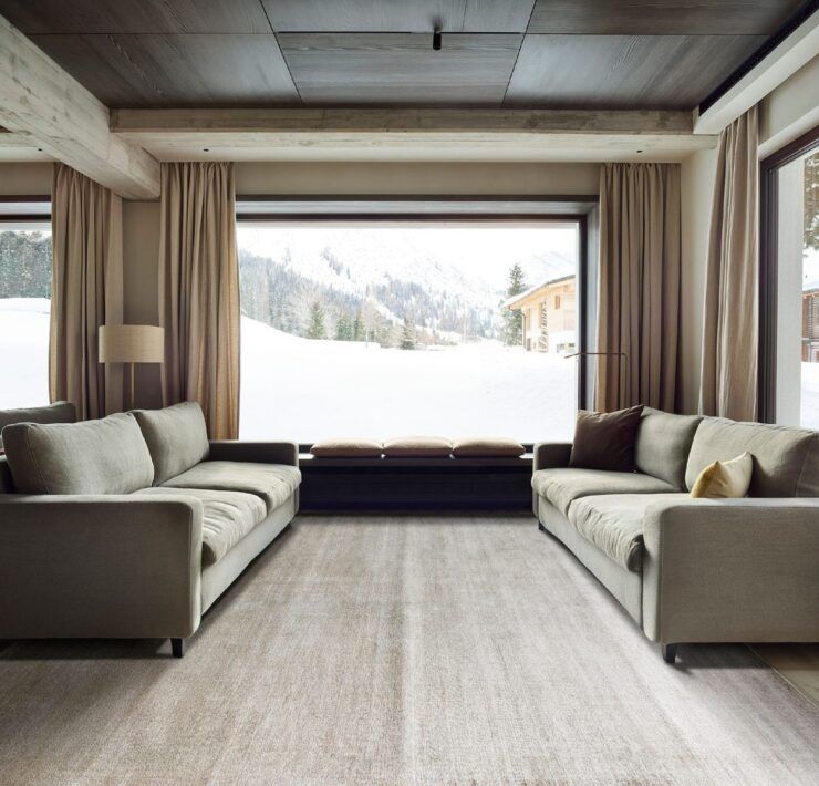 Alfombra Frizzantino de G.T.DESIGN en tono gris perla en una sala de chalet con dos sofás y ventanales con vista a la nieve
