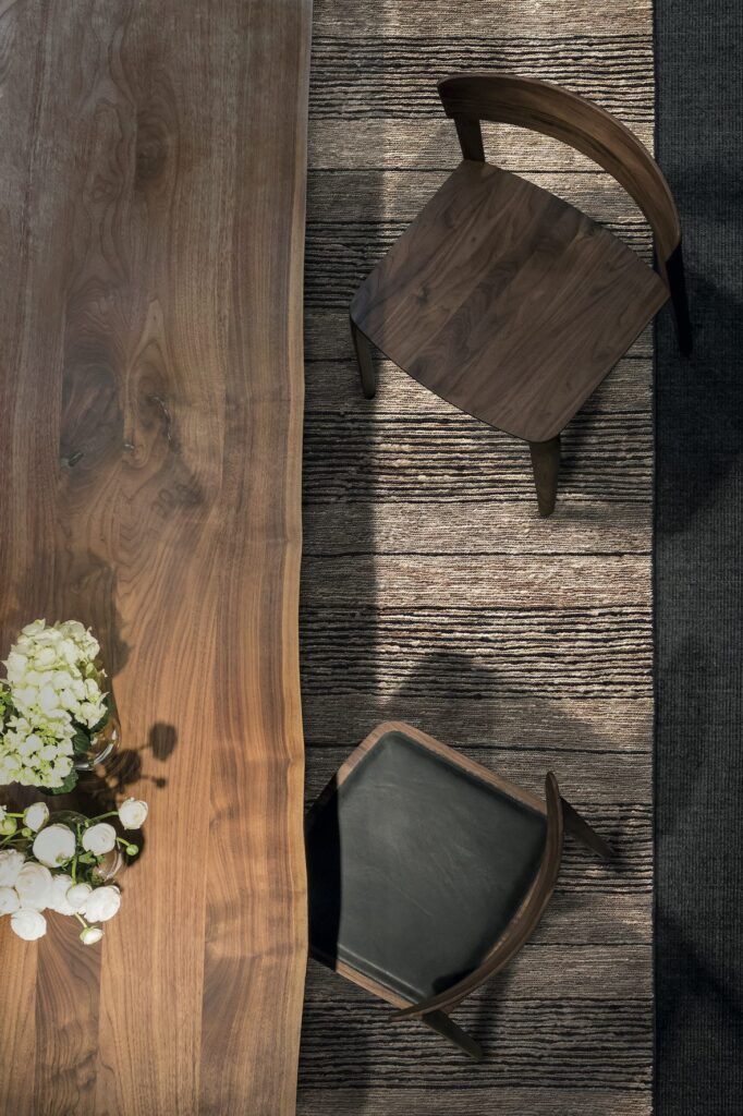 Vista cenital de la alfombra de otoño Himalayan Skin de G.T.DESIGN en fibra de ortiga bajo una mesa de madera de nogal y sillas