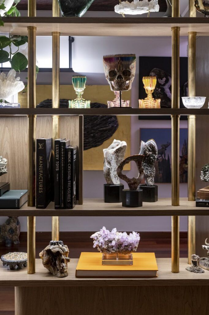 Celosía de madera con postes de bronce que funciona como repisa para minerales, calaveras escultóricas y libros en Casa Mineral
