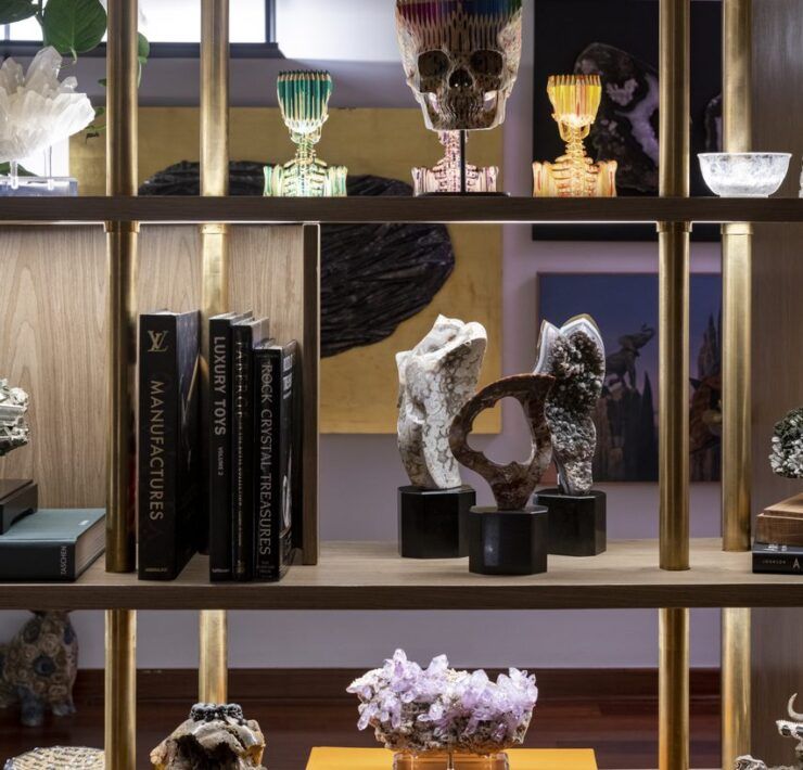 Celosía de madera con postes de bronce que funciona como repisa para minerales, calaveras escultóricas y libros en Casa Mineral