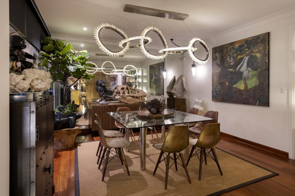 diseño de interiores en Lima de Comedor de Casa Mineral con mesa de vidrio cuadrada, sillas de bronce y madera, y lámpara escultórica de cuarzo
