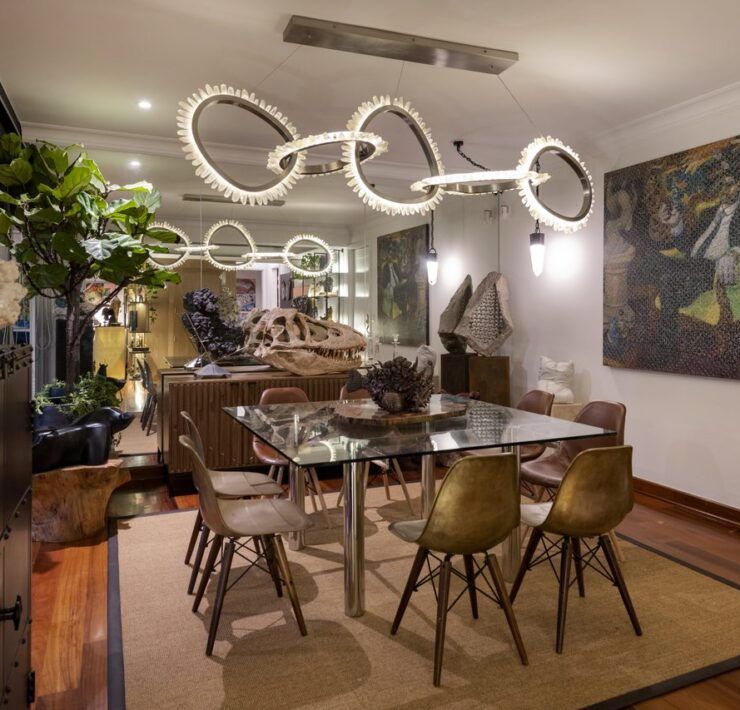 Comedor de Casa Mineral con mesa de vidrio cuadrada, sillas de bronce y madera, y lámpara escultórica de cuarzo