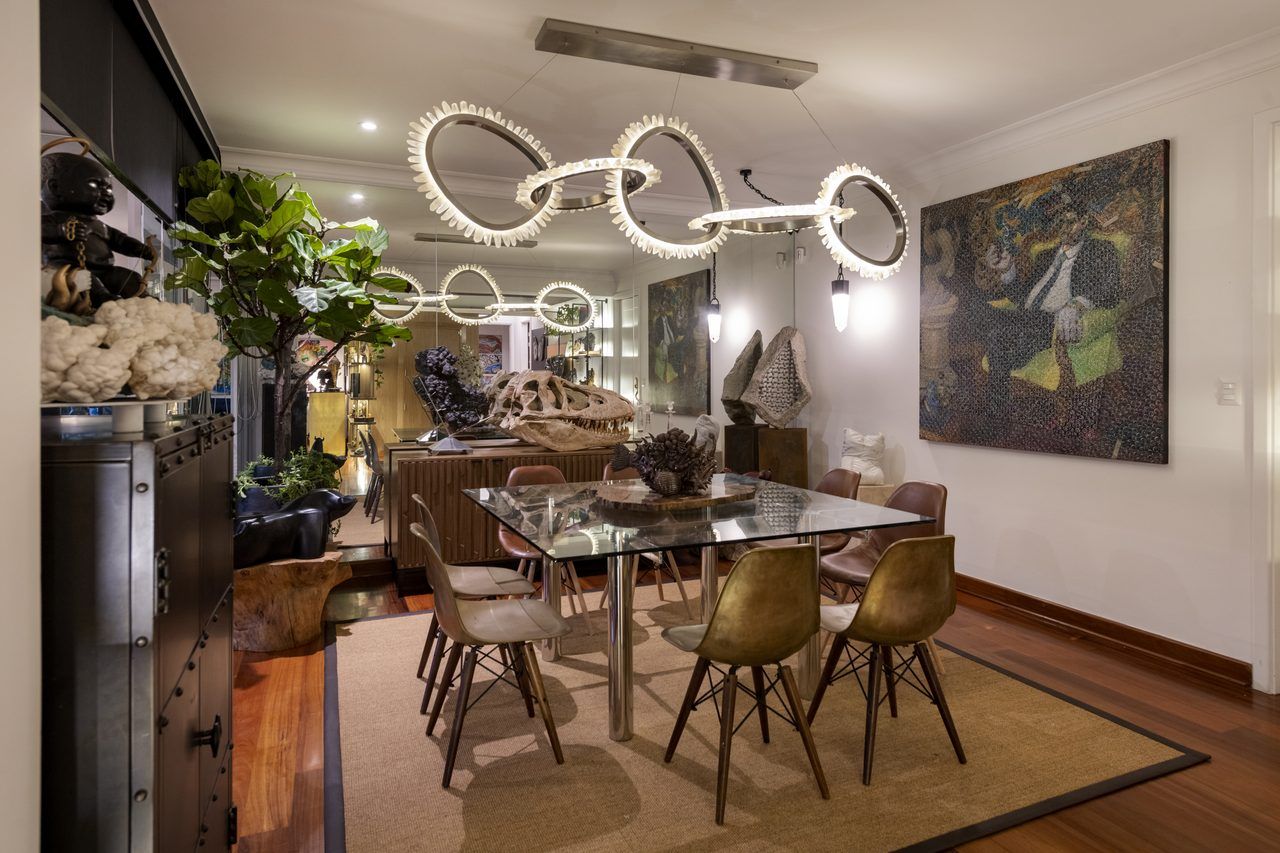 Comedor de Casa Mineral con mesa de vidrio cuadrada, sillas de bronce y madera, y lámpara escultórica de cuarzo