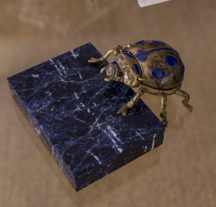 Escarabajo de bronce con incrustaciones azules sobre caja de piedra azul veteada en Casa Mineral