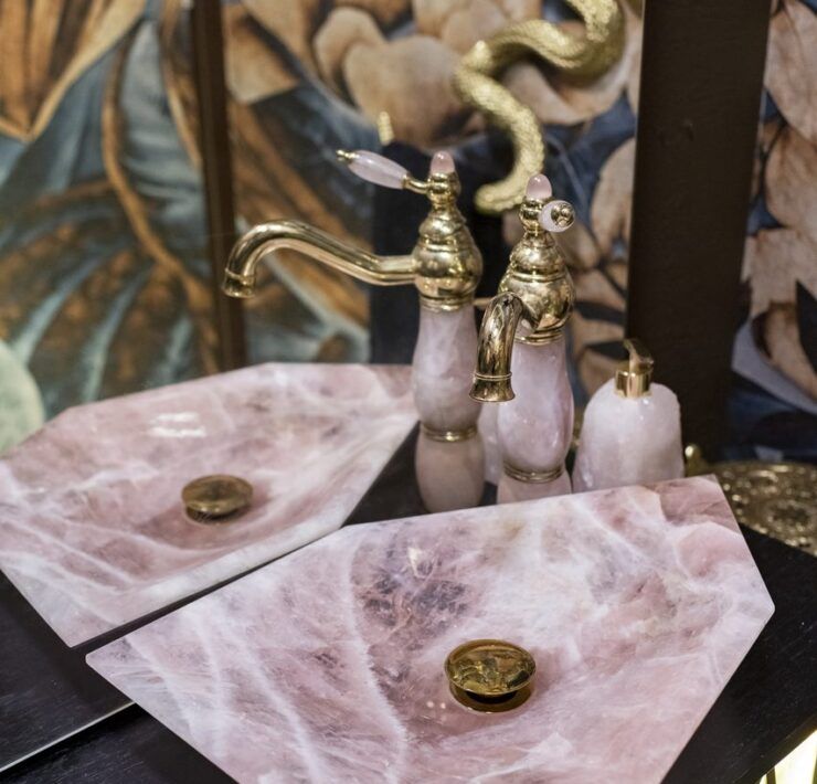 Lavabos de cuarzo rosa con grifería dorada y manerales de cuarzo en el baño de visitas de Casa Mineral