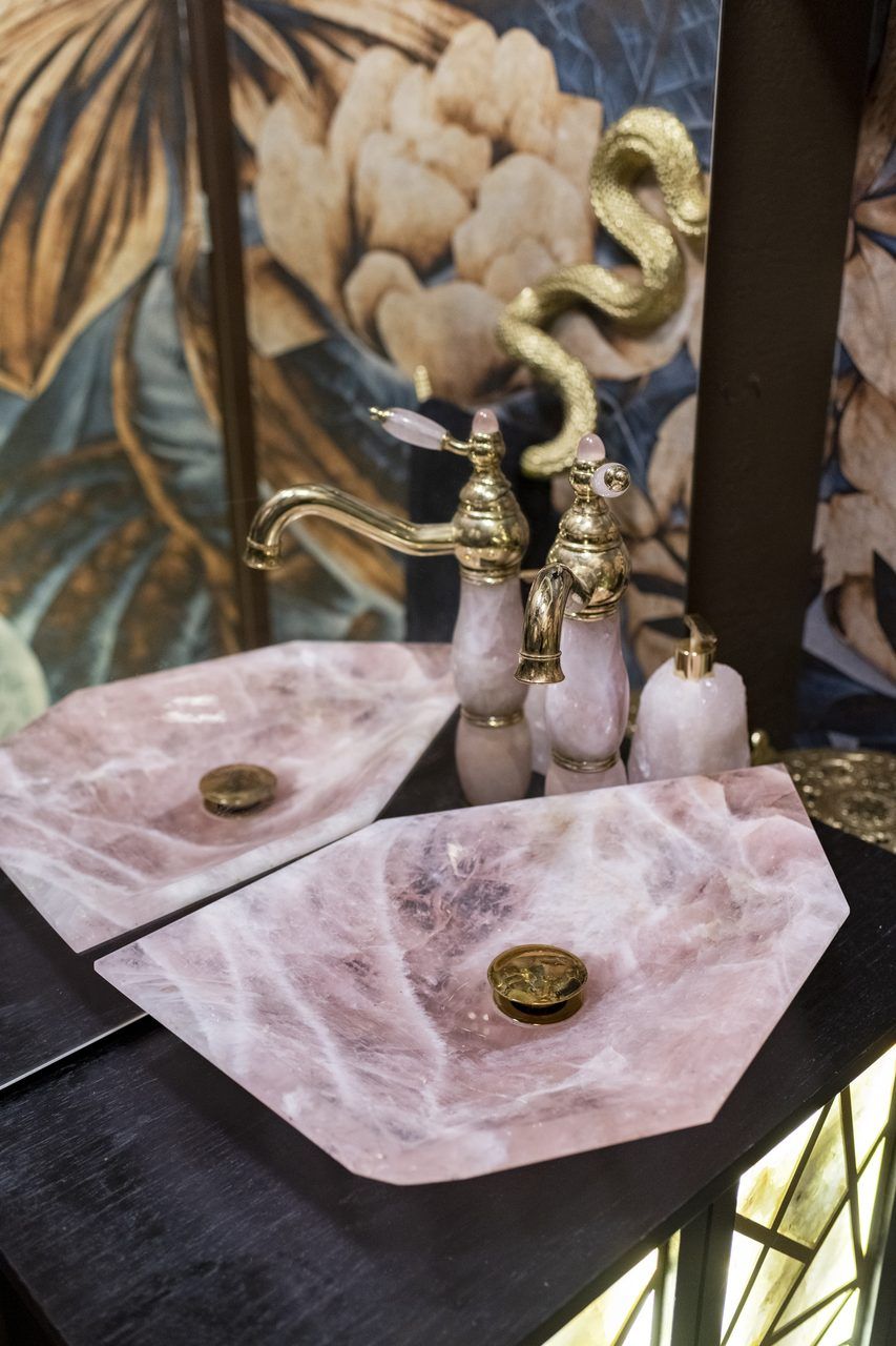 Lavabos de cuarzo rosa con grifería dorada y manerales de cuarzo en el baño de visitas de Casa Mineral