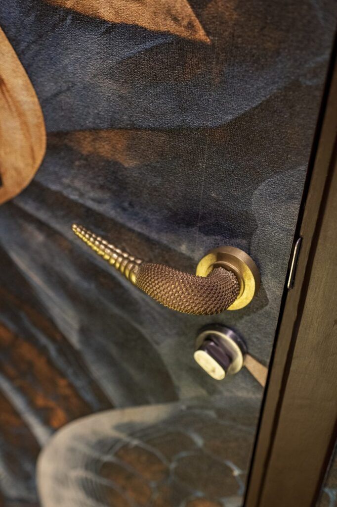 Manija de puerta dorada con textura de piel de serpiente y punta de cascabel en Casa Mineral