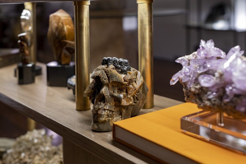 Repisa de Casa Mineral con calavera tallada en mineral, racimo de amatista sobre base de acrílico y libro naranja