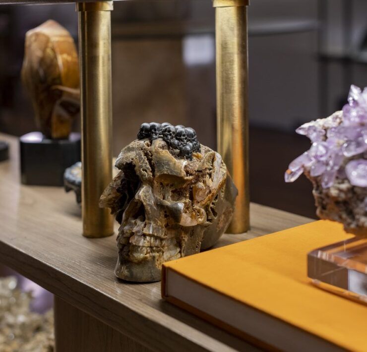 Repisa de Casa Mineral con calavera tallada en mineral, racimo de amatista sobre base de acrílico y libro naranja