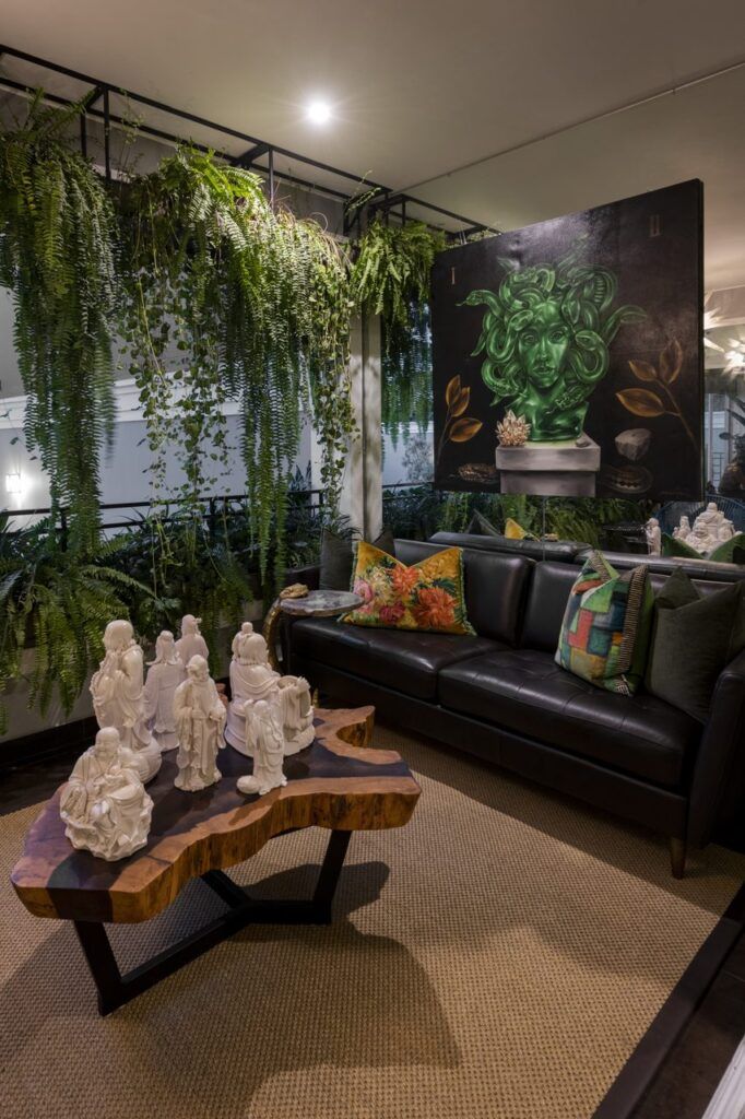 Terraza de Casa Mineral con helechos colgantes, sofá de piel negro, cuadro de Medusa y muro de espejo que refleja la vegetación