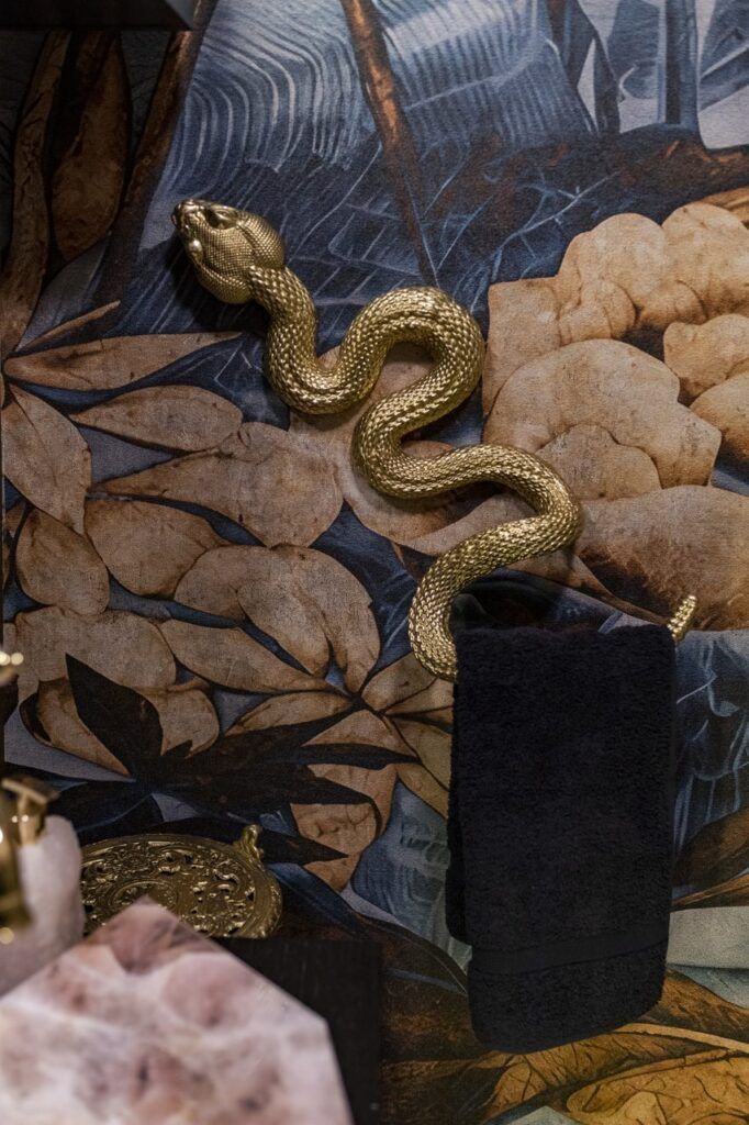 Toallero dorado en forma de serpiente sobre papel tapiz botánico en el baño de visitas de Casa Mineral