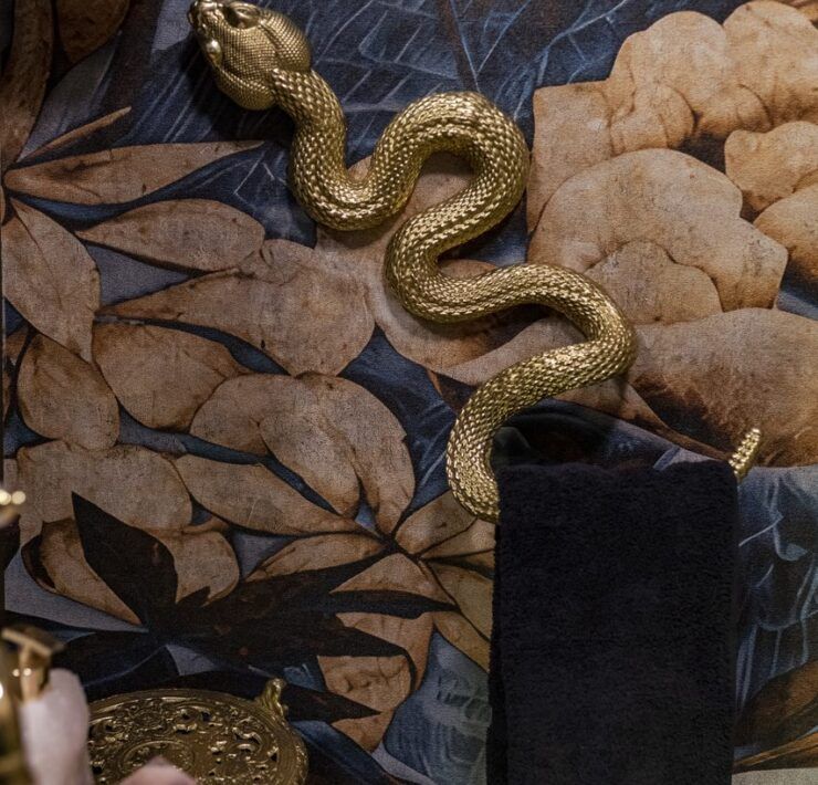 Toallero dorado en forma de serpiente sobre papel tapiz botánico en el baño de visitas de Casa Mineral