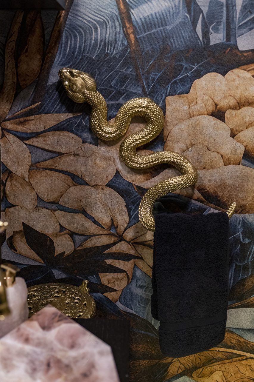Toallero dorado en forma de serpiente sobre papel tapiz botánico en el baño de visitas de Casa Mineral